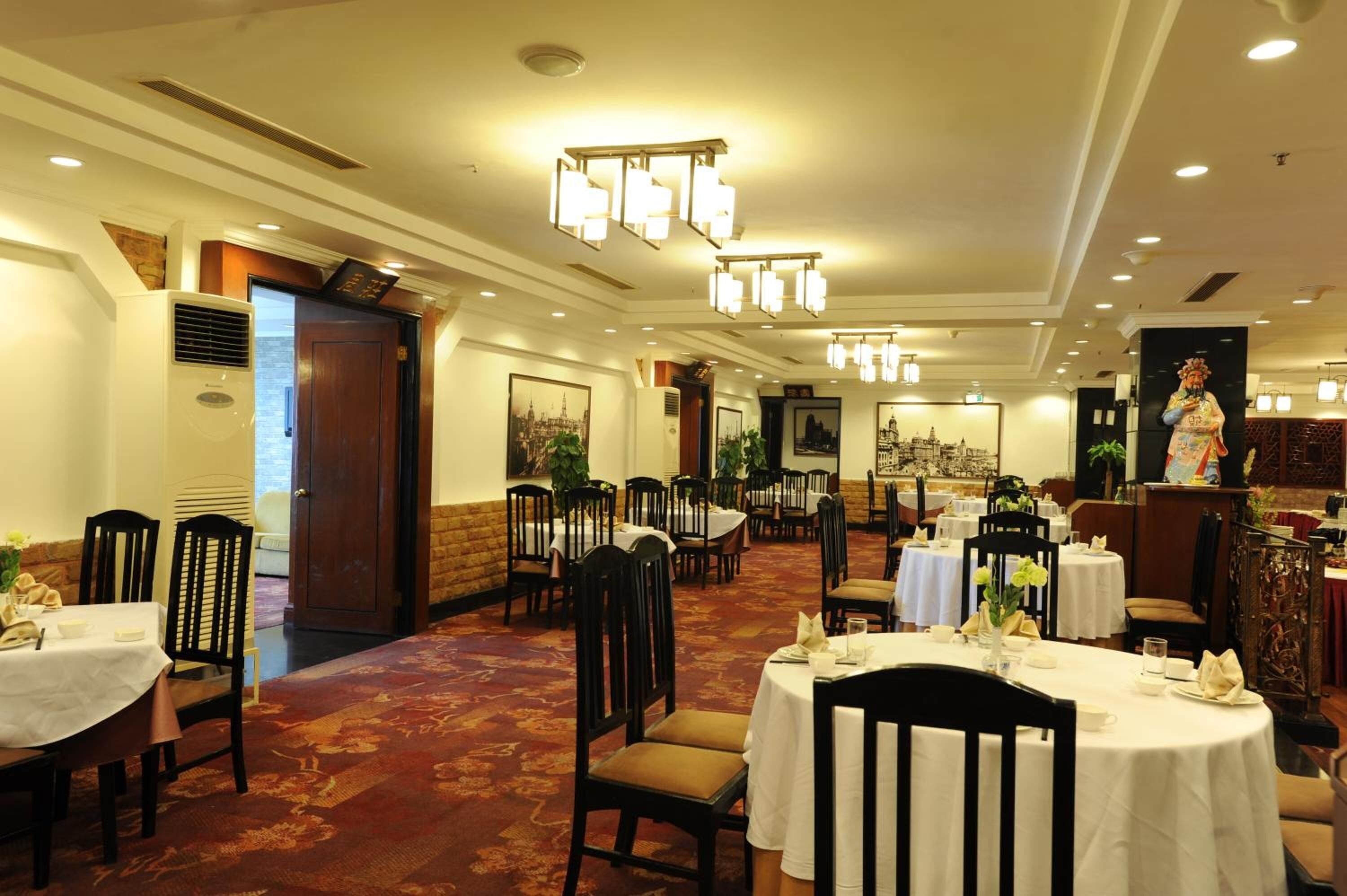 A hotel dining area with multiple tables and chairs, chandeliers, and a large statue.