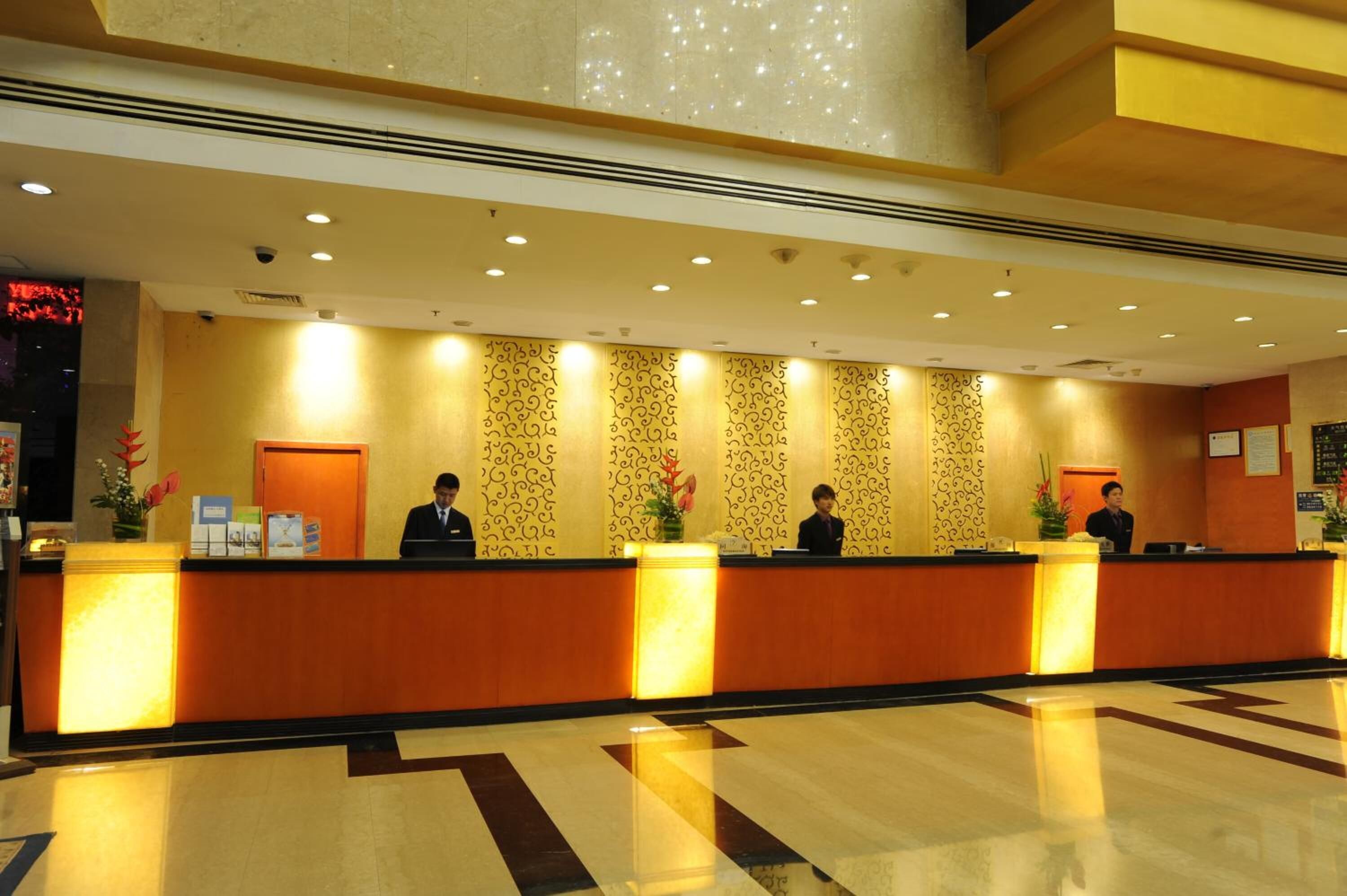 A hotel reception area with a long reception desk, three staff members, and patterned wallpaper.