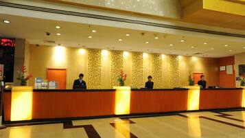 A hotel reception area with a long reception desk, three staff members, and patterned wallpaper.