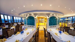 A spacious restaurant with high ceilings, large windows, and a central bar area. Tables are neatly set with white tablecloths and gold napkins. - Kunming Jin Jiang Hotel (Kunming)