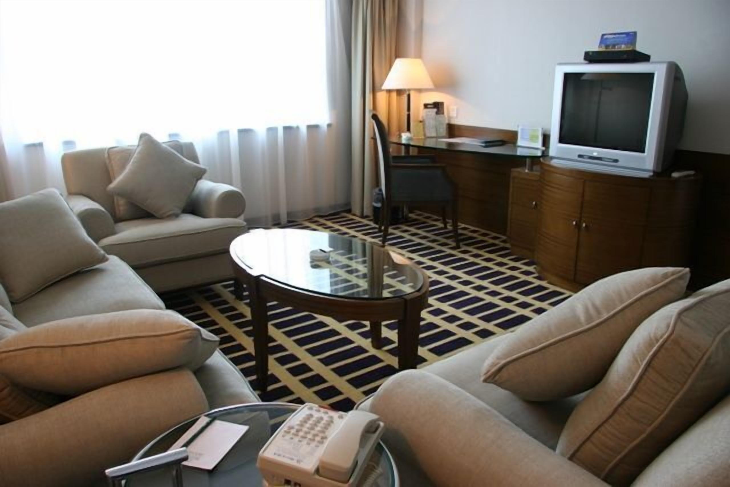 A hotel room with a sofa, armchair, a glass coffee table, a television, and a telephone.