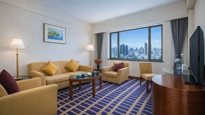 A hotel room with a sofa, armchairs, a coffee table, a TV, and a large window with a city view. - Kunming Jin Jiang Hotel (Kunming)