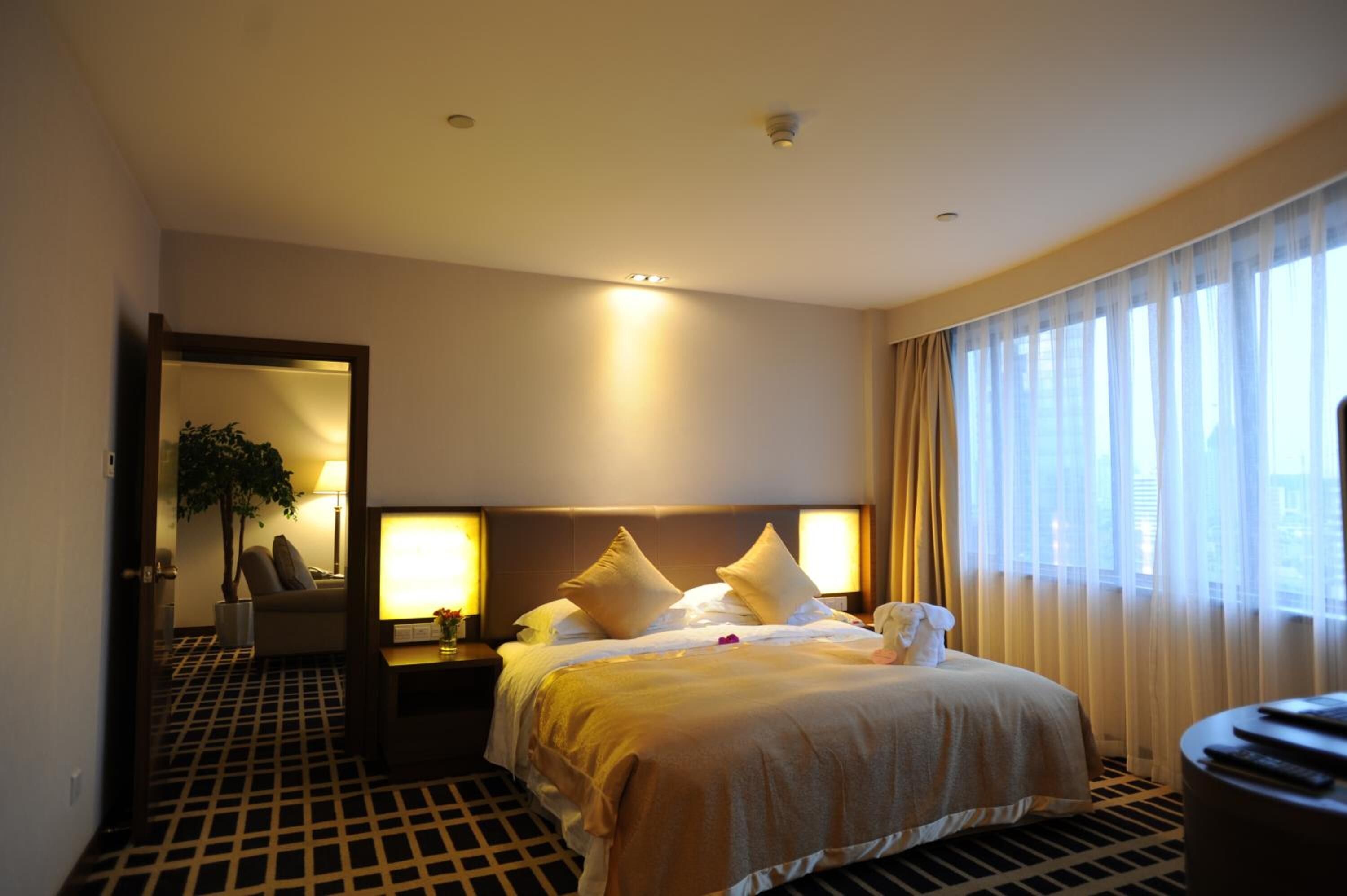 A hotel room with a bed, bedside lamps, a nightstand, a chair, and a large window with curtains.