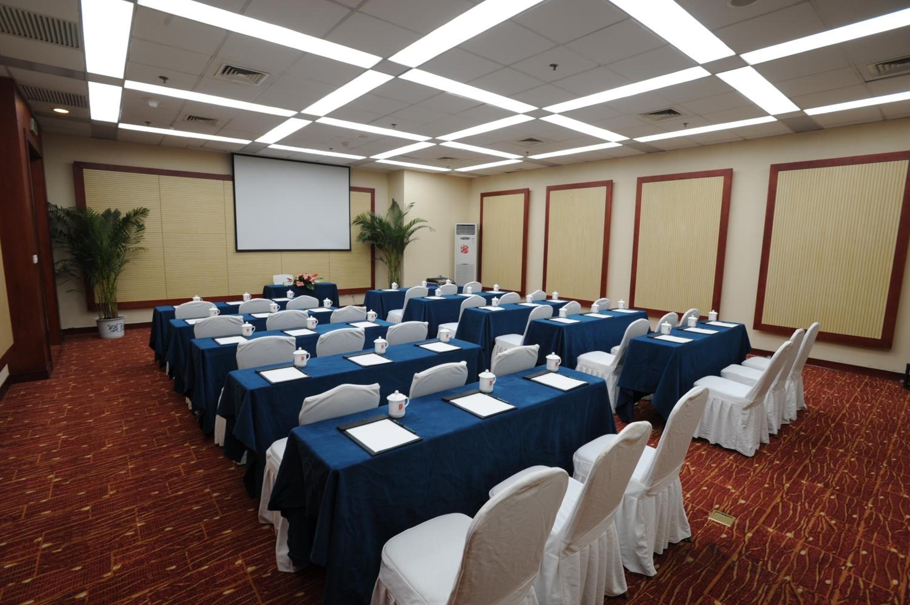 A conference room with rows of tables, chairs, and a projector screen.