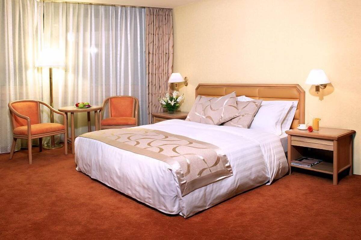 Una habitación de hotel con una cama grande, dos sillas, una mesita con fruta, una lámpara y una mesita de noche con lámpara y teléfono.