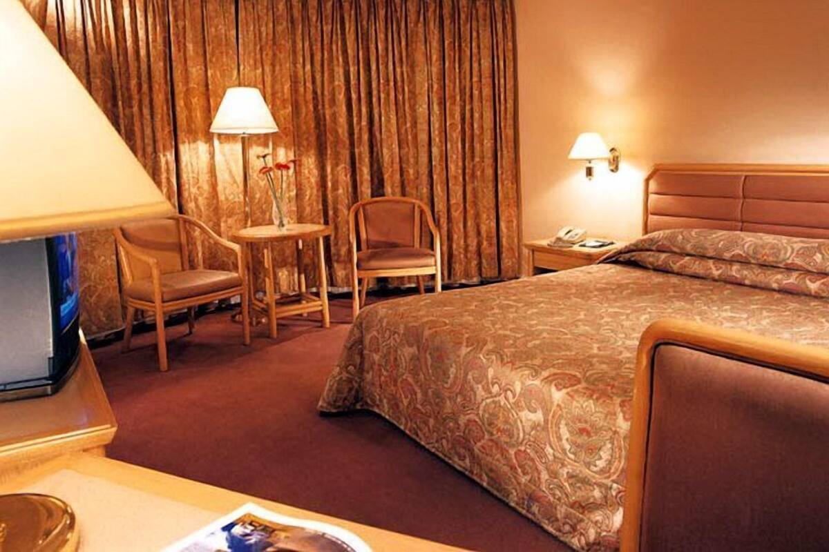 Habitación de hotel con cama, dos sillas, una mesita, una lámpara y un teléfono.