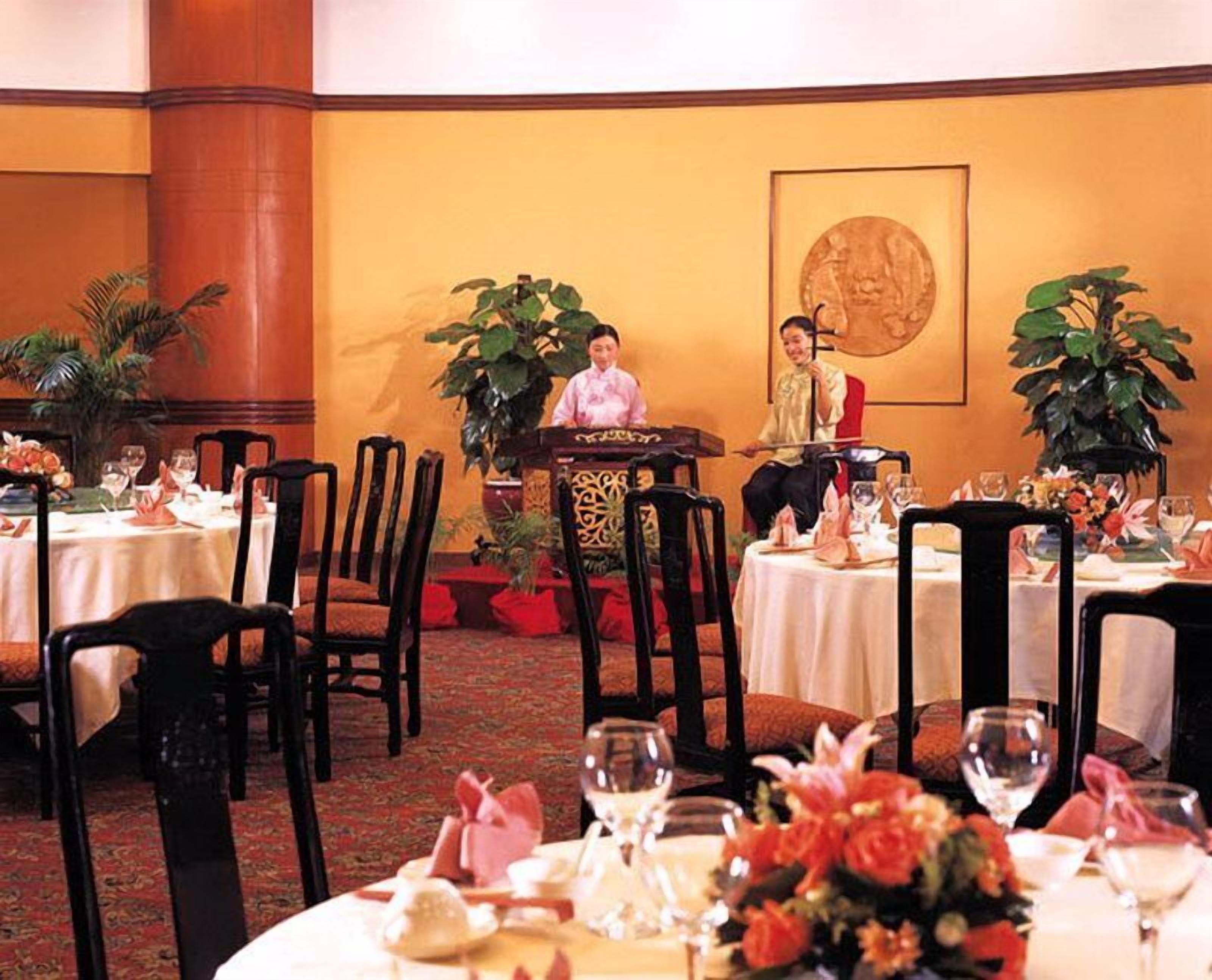 Comedor con mesas redondas dispuestas para una comida, sillas y plantas en macetas.