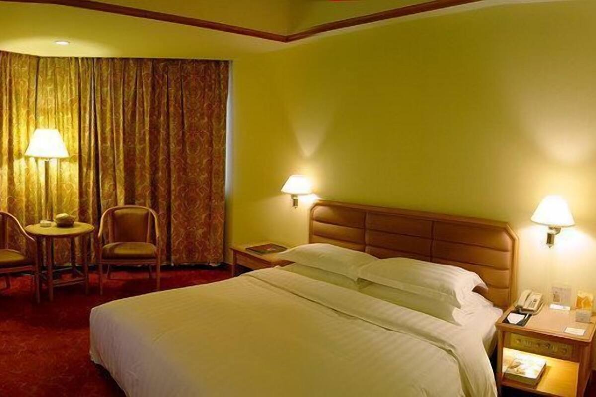 Una habitación de hotel con una cama, dos sillas, una mesita, un escritorio con una lámpara y una cortina.