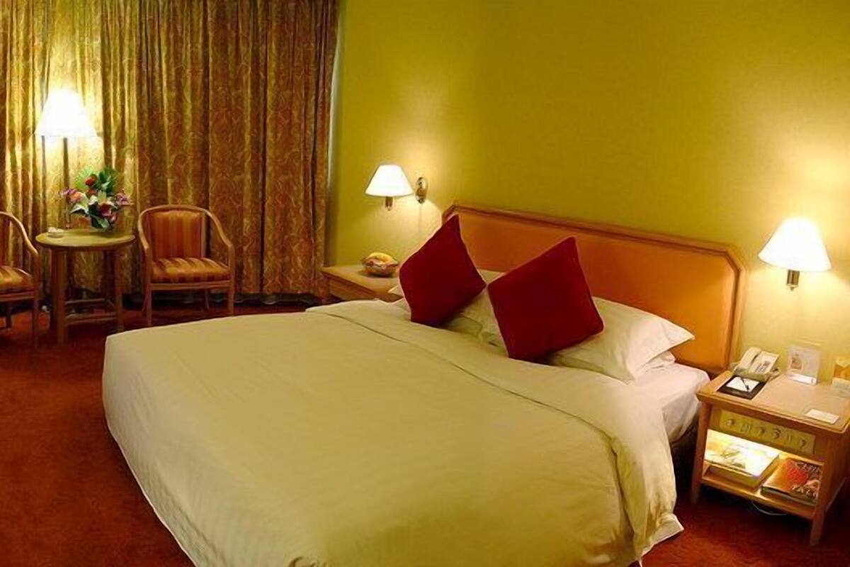 Habitación de hotel con una cama grande, dos sillas, una mesita con lámpara y televisión.