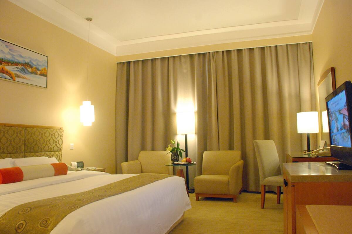 Quarto de hotel com uma cama grande, duas poltronas, uma escrivaninha com televisão e um quadro na parede.