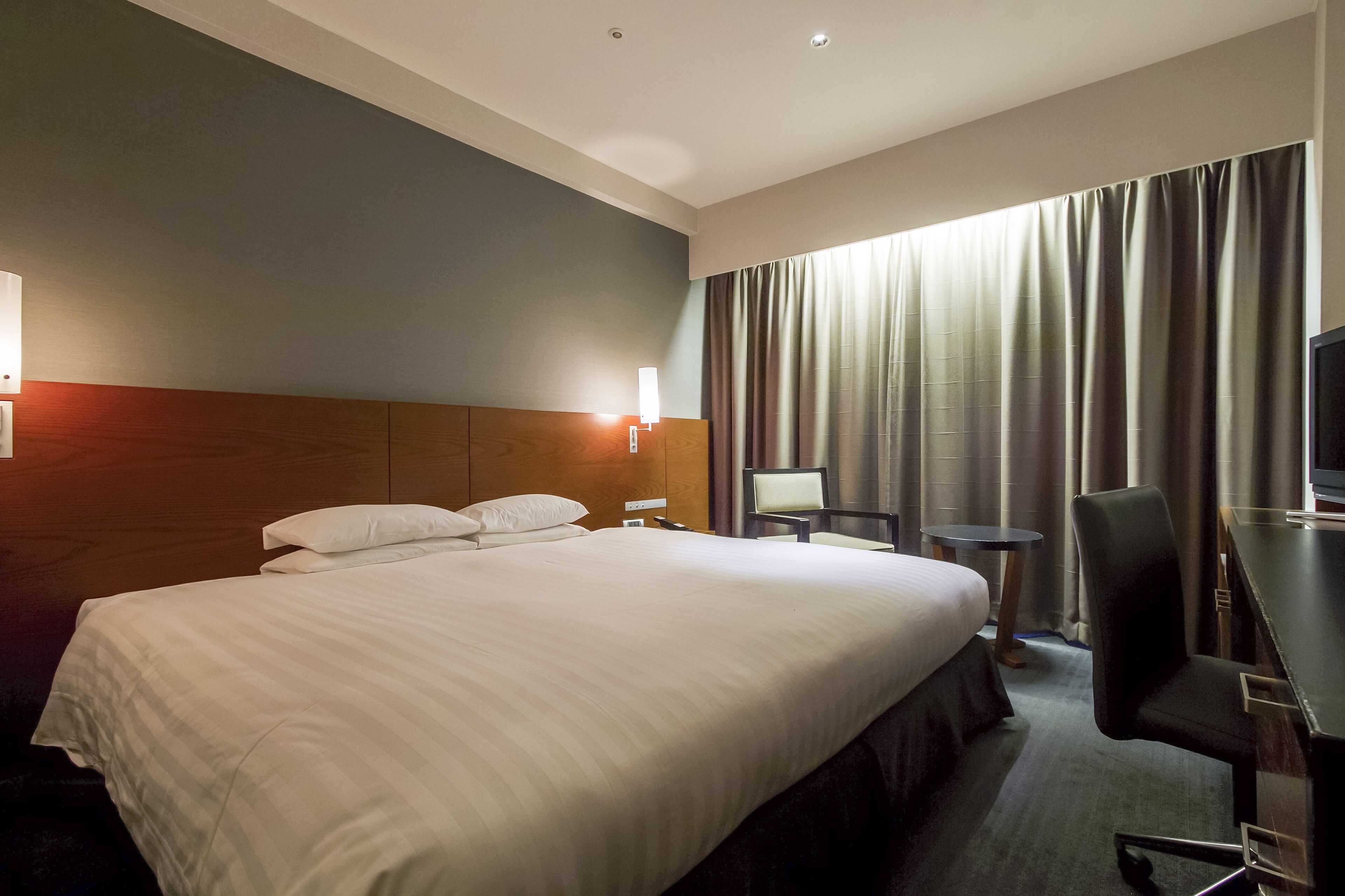 A hotel room with a large bed, a desk with a chair, a small table, and a TV.