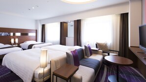 Ein Hotelzimmer mit zwei Betten, einer Schlafcouch, einem kleinen Tisch, einem Fernseher und einem großen Fenster mit Vorhängen.