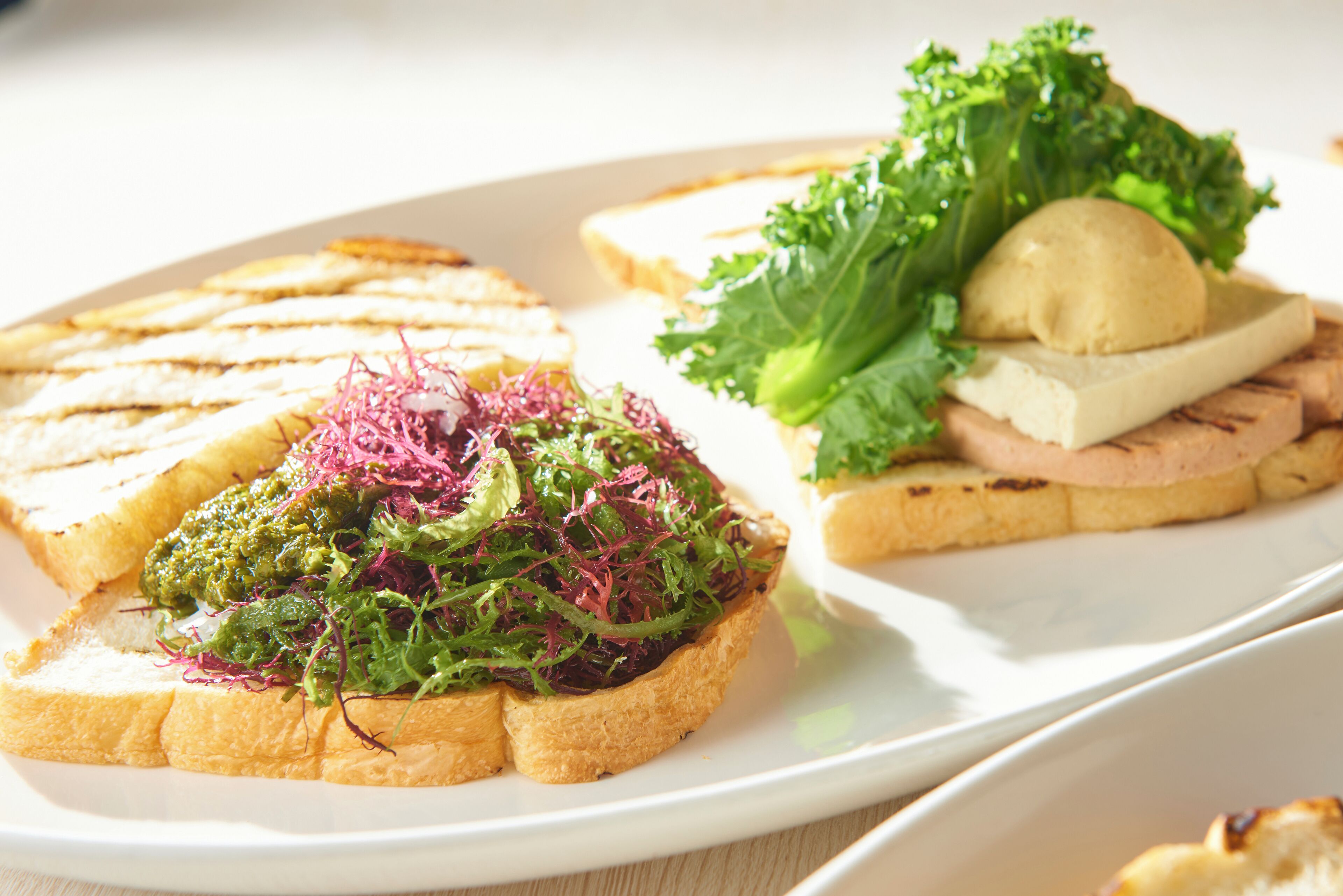 A plate with three types of sandwiches: one with greens, one with a meat topping, and one with a cheese and mushroom.