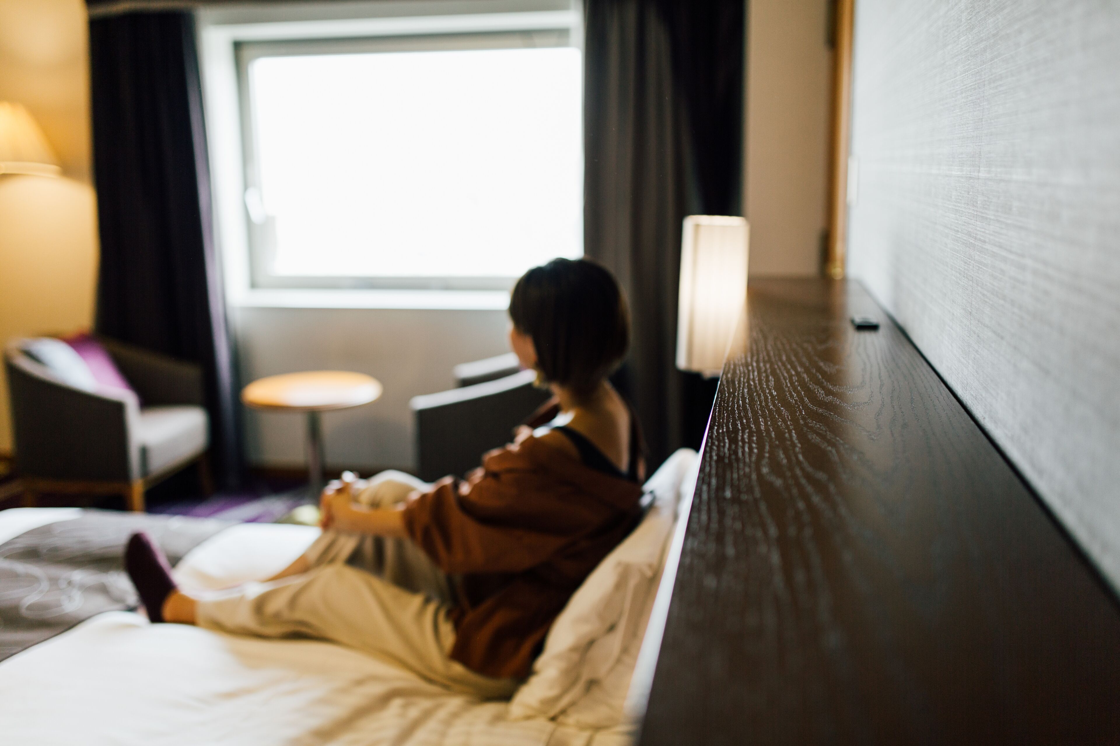 A hotel room with a bed, a chair, a small table, and a window.