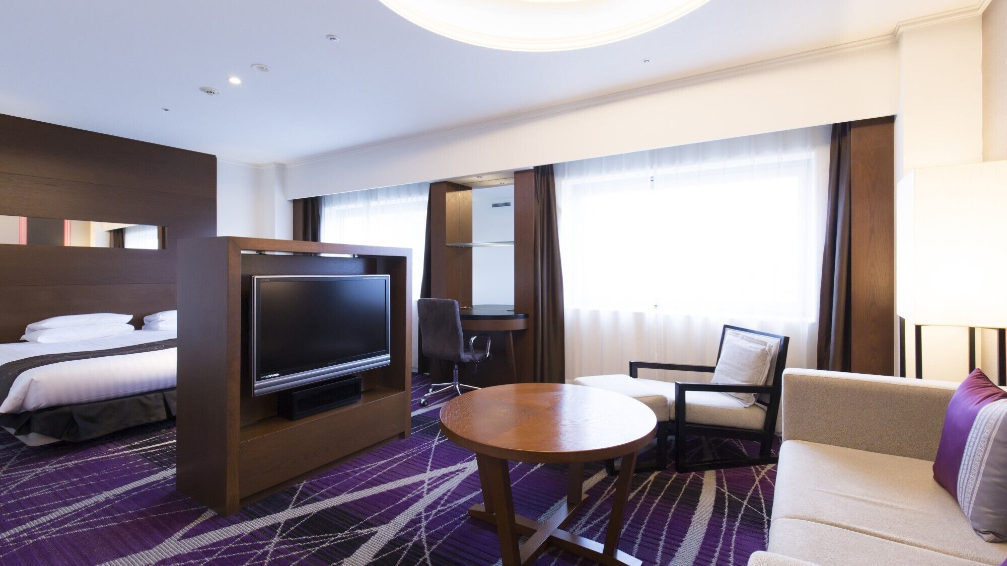 A hotel room with a bed, a TV, a desk, a chair, a sofa, and a round table.