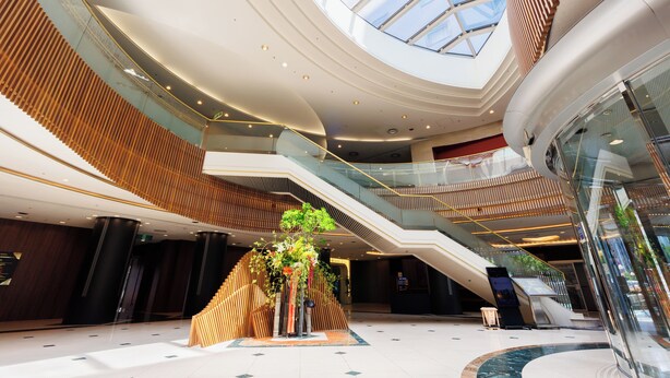 Ein modernes Interieur mit einem zentralen Atrium, Glasgeländern und einer Treppe zu den oberen Ebenen.