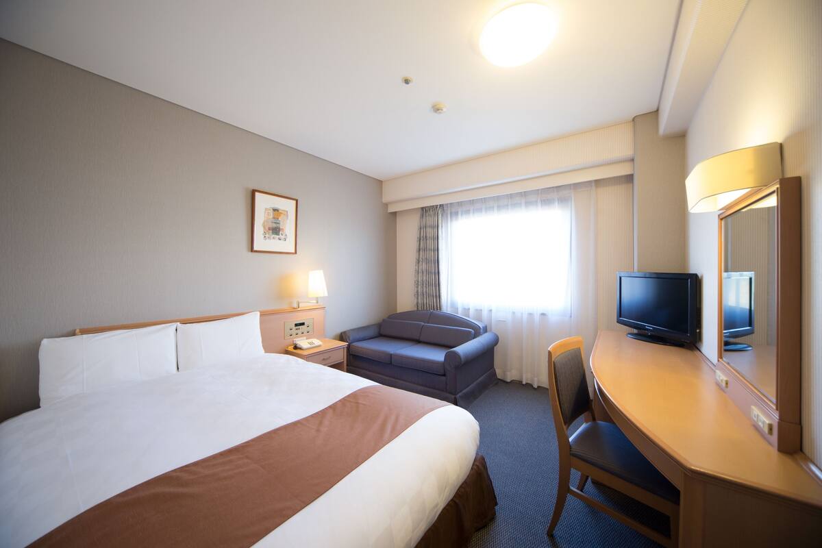 Een hotelkamer met een groot bed, een bureau met televisie, een stoel en een raam met gordijnen.