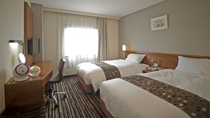 Habitación de hotel con dos camas, un escritorio con silla, televisión y ventana con cortinas.