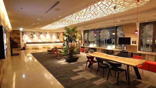 Un hall d’hôtel moderne comprenant un comptoir d’accueil, un espace salon et une grande fenêtre donnant sur la ville.