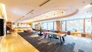 Un hall d’entrée spacieux au design moderne, doté d’un long comptoir de réception, de coins salons confortables et de grandes fenêtres offrant une vue sur la ville.