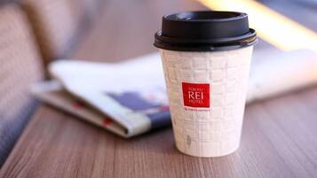 A disposable coffee cup with a Tokyo Rei Hotel logo, placed on a wooden surface with a blurred magazine or booklet in the background.