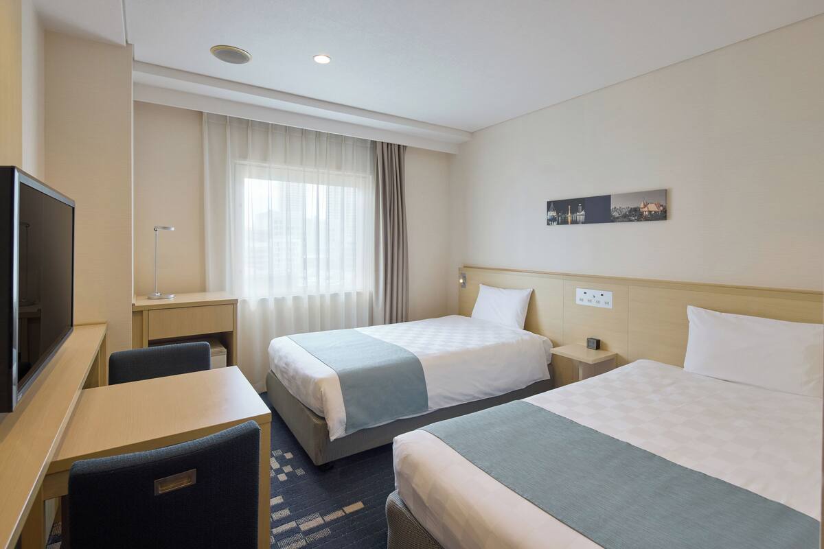 Een hotelkamer met twee bedden, een bureau, een televisie en een raam met gordijnen.