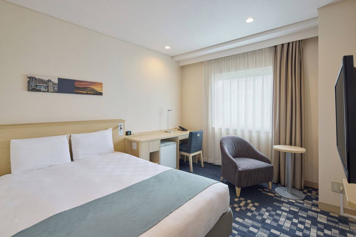 Een hotelkamer met een bed, bureau, stoel, televisie en een schilderij aan de muur.
