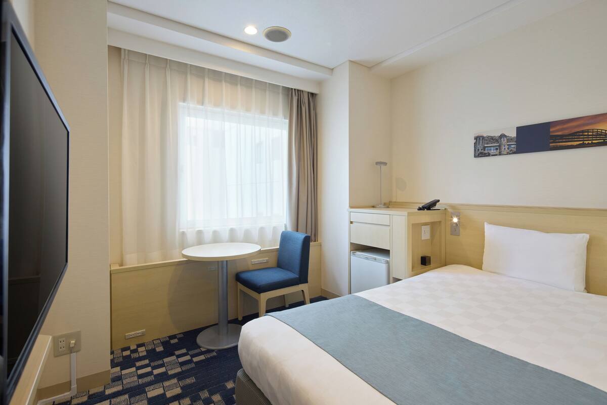 Een hotelkamer met een bed, een bureau met stoel, een televisie en een raam met gordijnen.