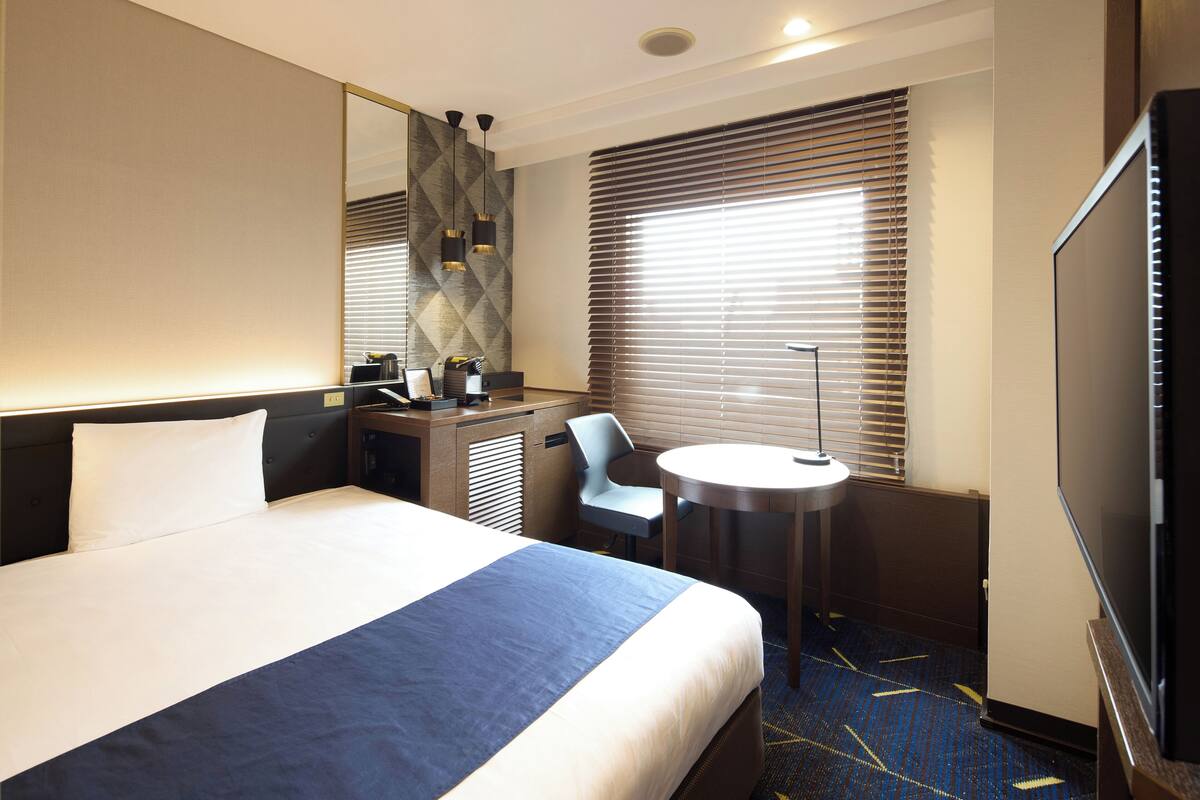 Een hotelkamer met een groot bed, een bureau, een stoel, een ronde tafel en een televisie.