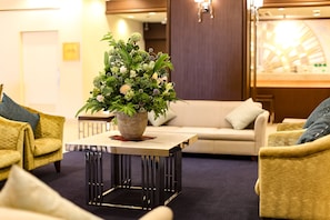 Un hall d’entrée avec une table centrale, un canapé et deux fauteuils. Un grand arrangement floral est posé sur la table.