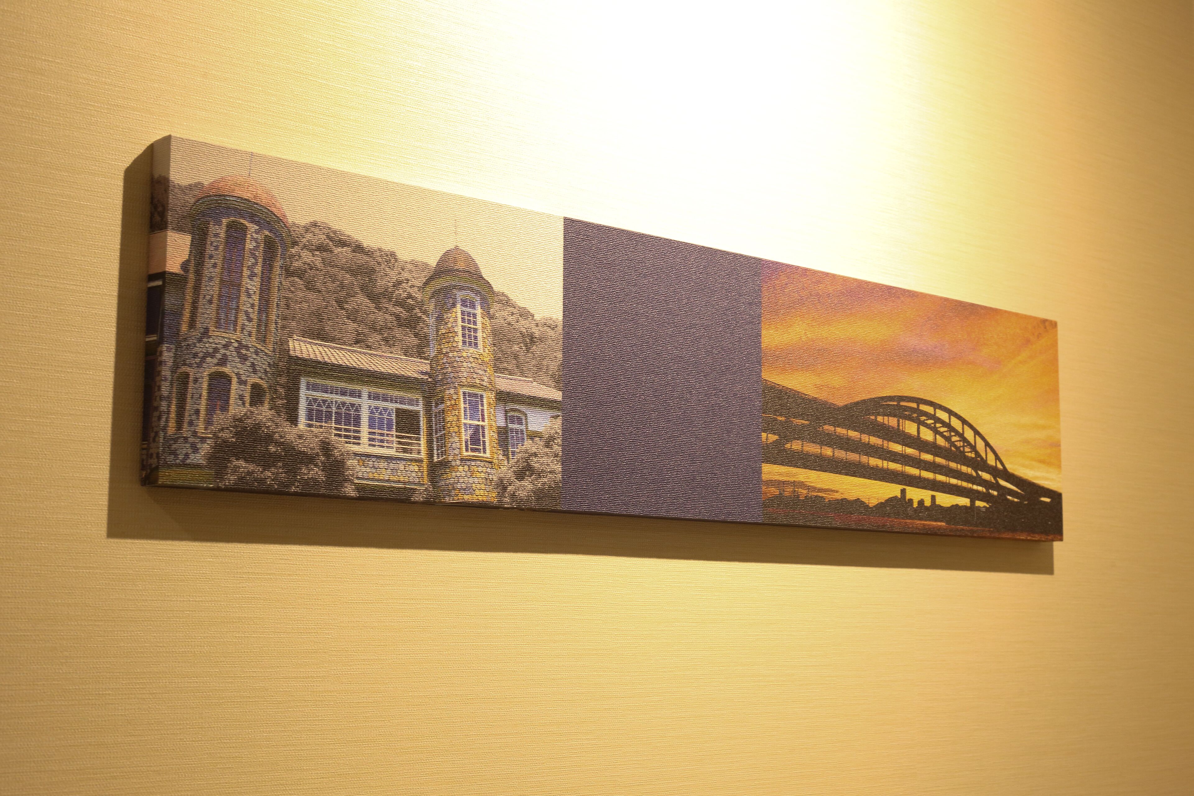 A wall-mounted artwork depicting architectural structures and a bridge against a sunset backdrop.