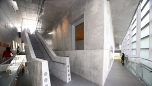 Un interior moderno con una escalera central, barandillas de vidrio y piso de baldosas.