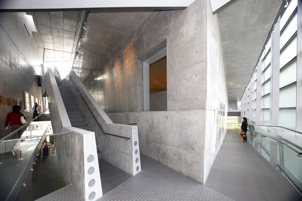 Un intérieur moderne avec un escalier central, des rampes en verre et un sol carrelé.