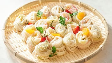 Una cesta tejida con alimentos ordenados, probablemente un plato de fideos asiático, adornado con hierbas y pequeñas frutas.