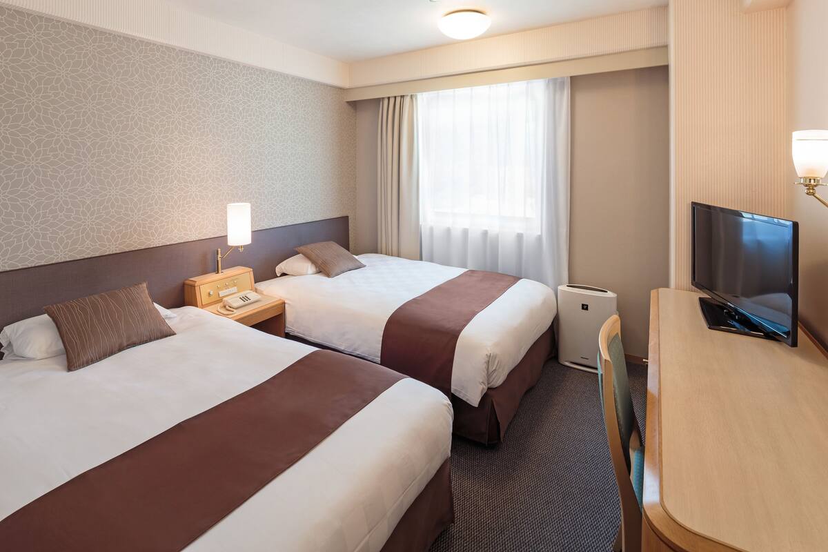 A hotel room with two beds, a desk, a television, and a telephone.