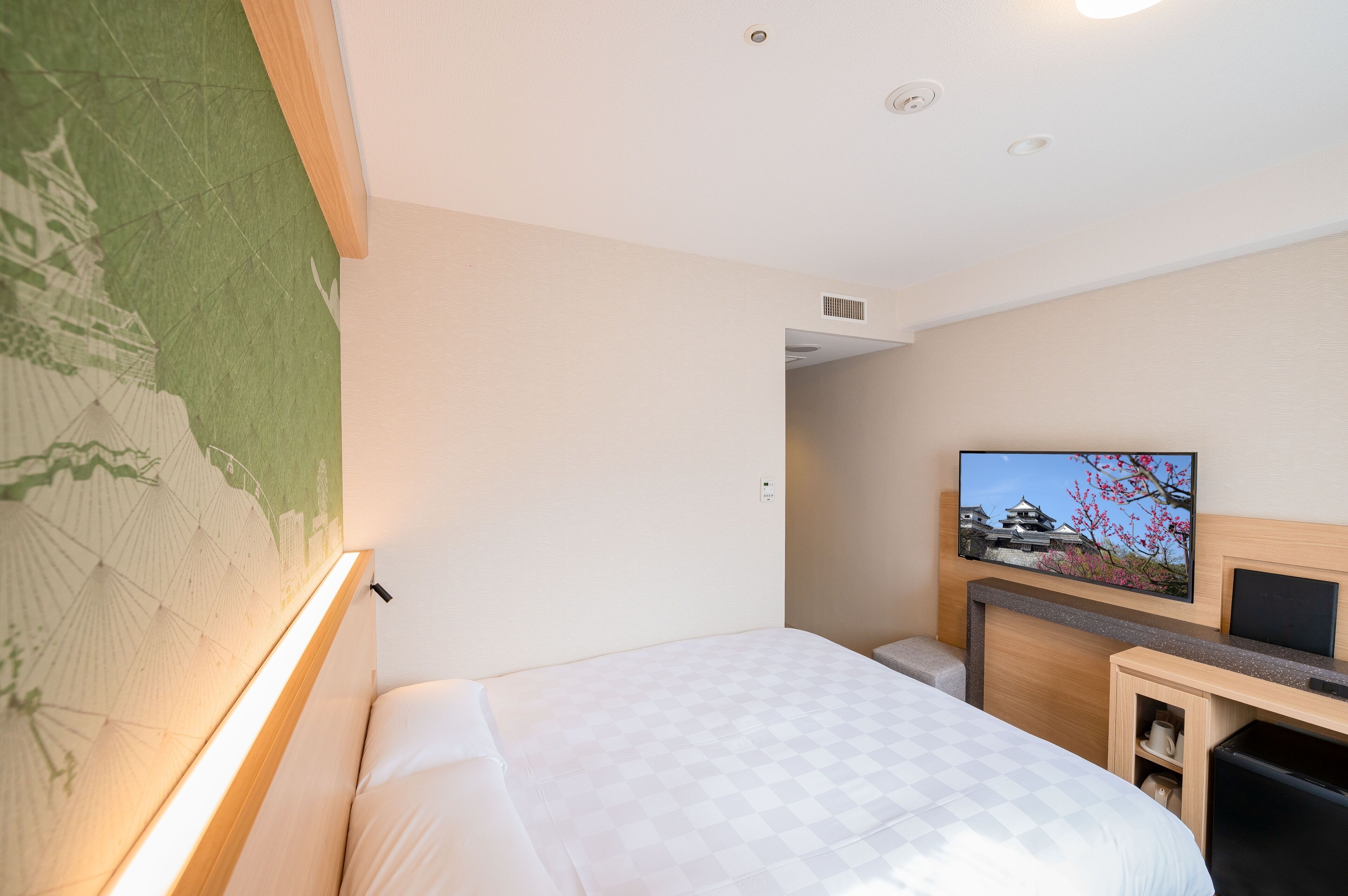 A hotel room with a bed, a television mounted on the wall, and a map on the wall.