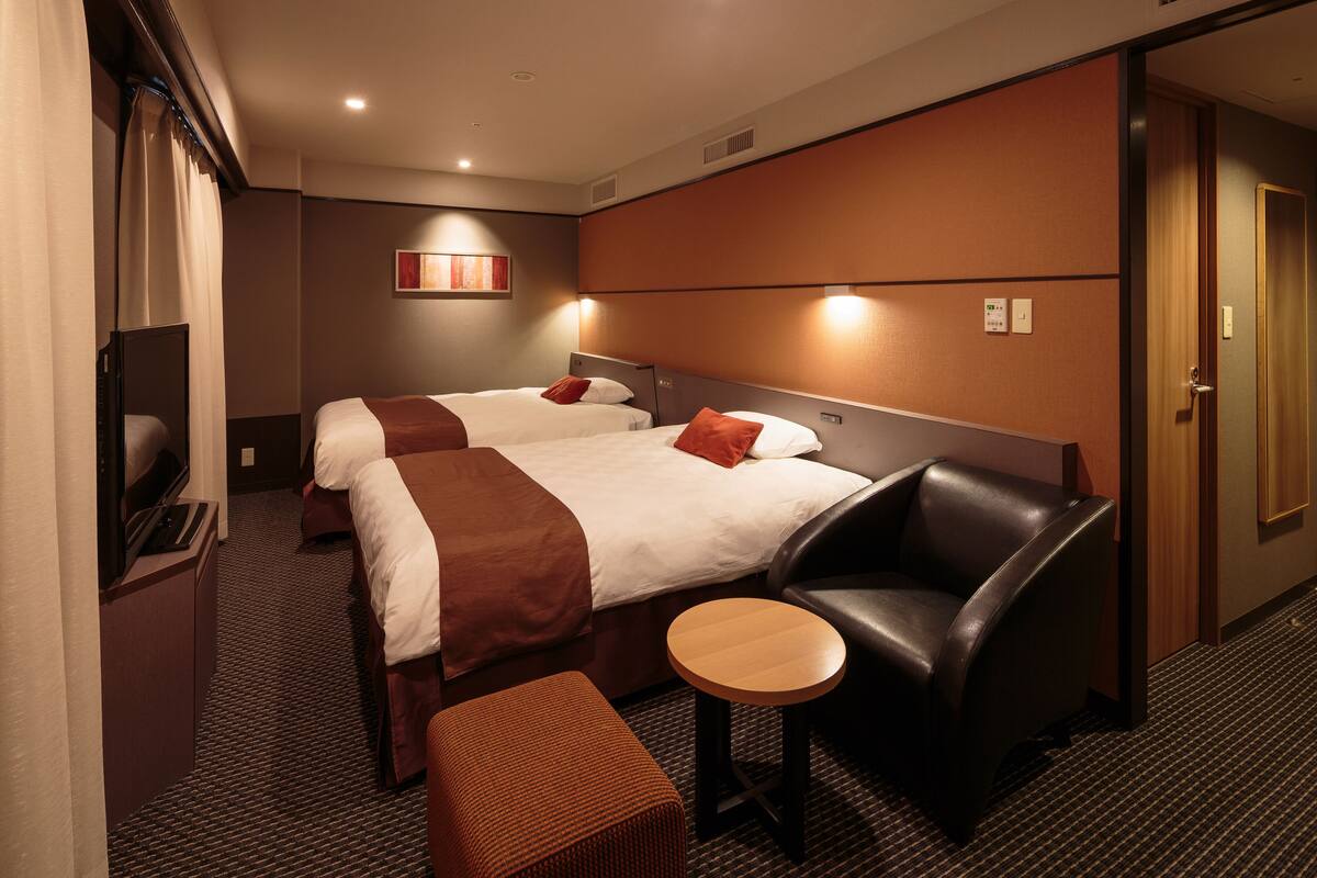 A hotel room with two beds, a TV, a desk, and a chair.