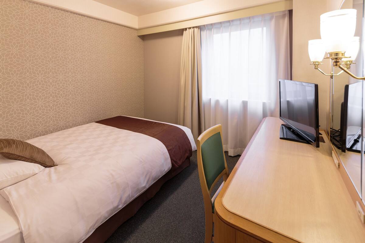 A hotel room with two beds, a desk, a chair, a TV, and a window with curtains.
