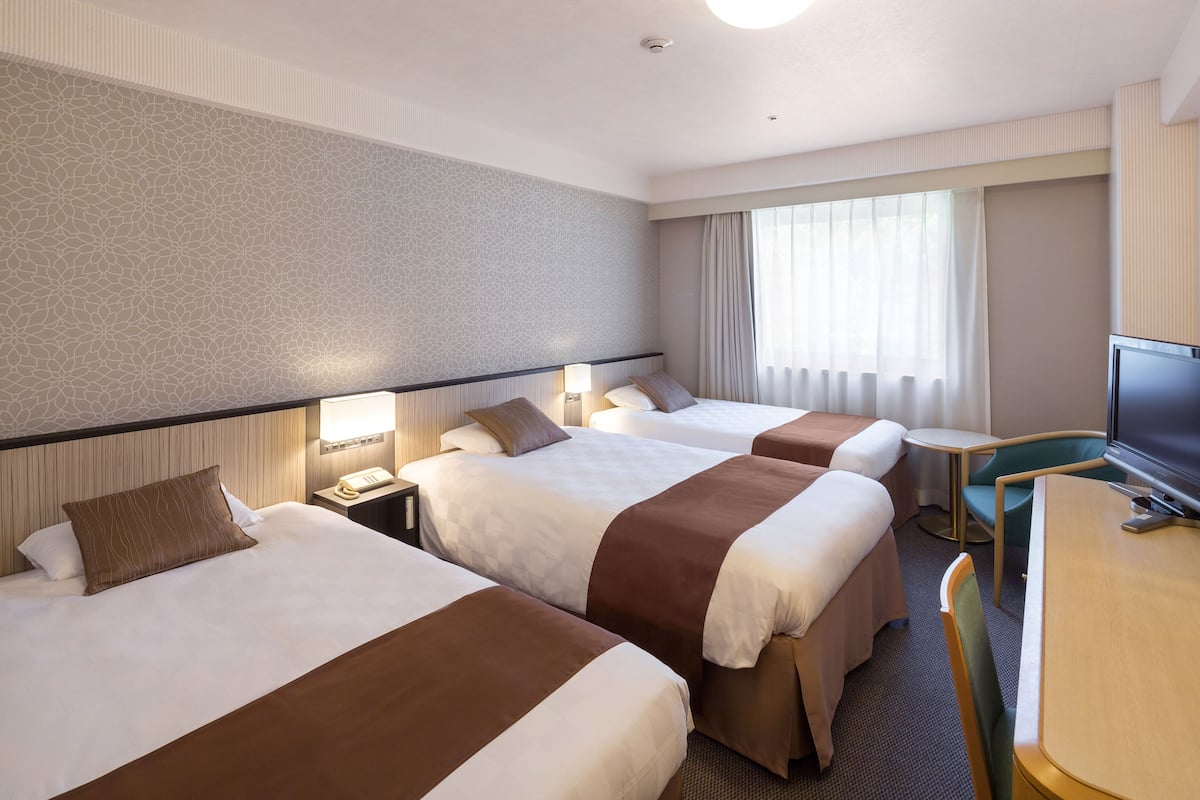 A hotel room with three beds, a desk, a television, and a window with curtains.