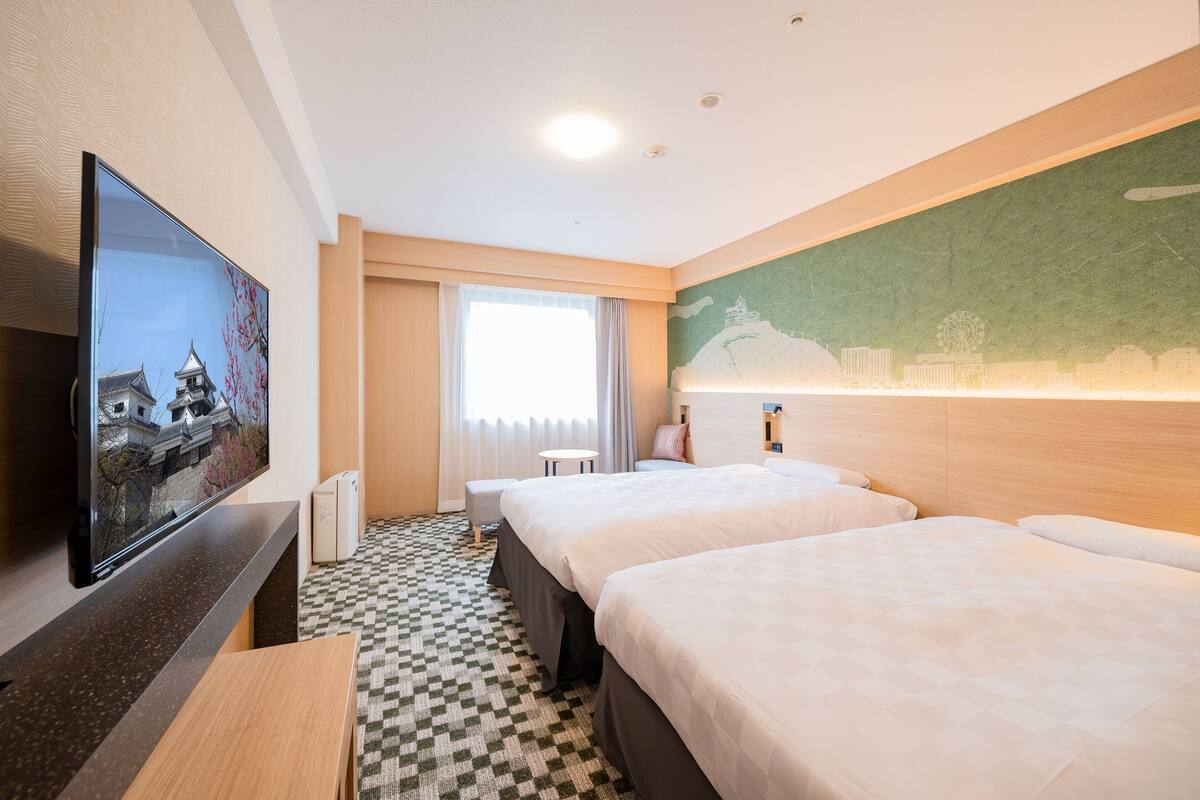 A hotel room with two beds, a flat-screen TV, a small table, and a window with curtains.