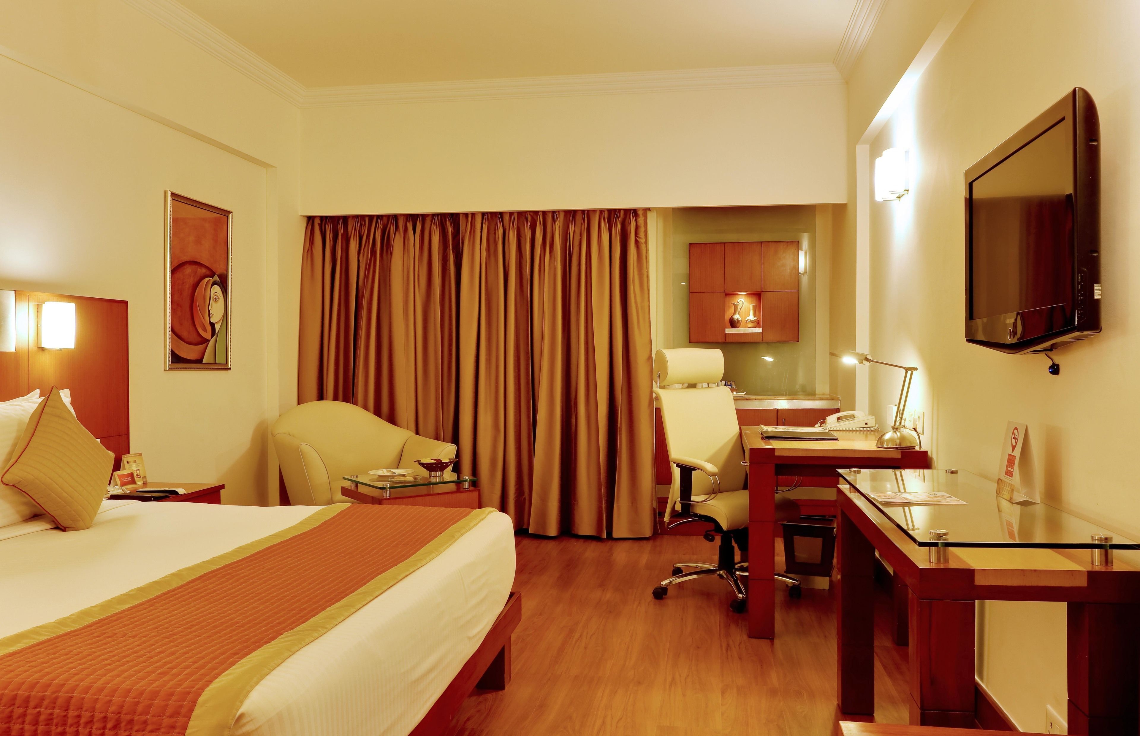 A hotel room with a large bed, a desk, a chair, a television, and a bathroom visible through a curtain.