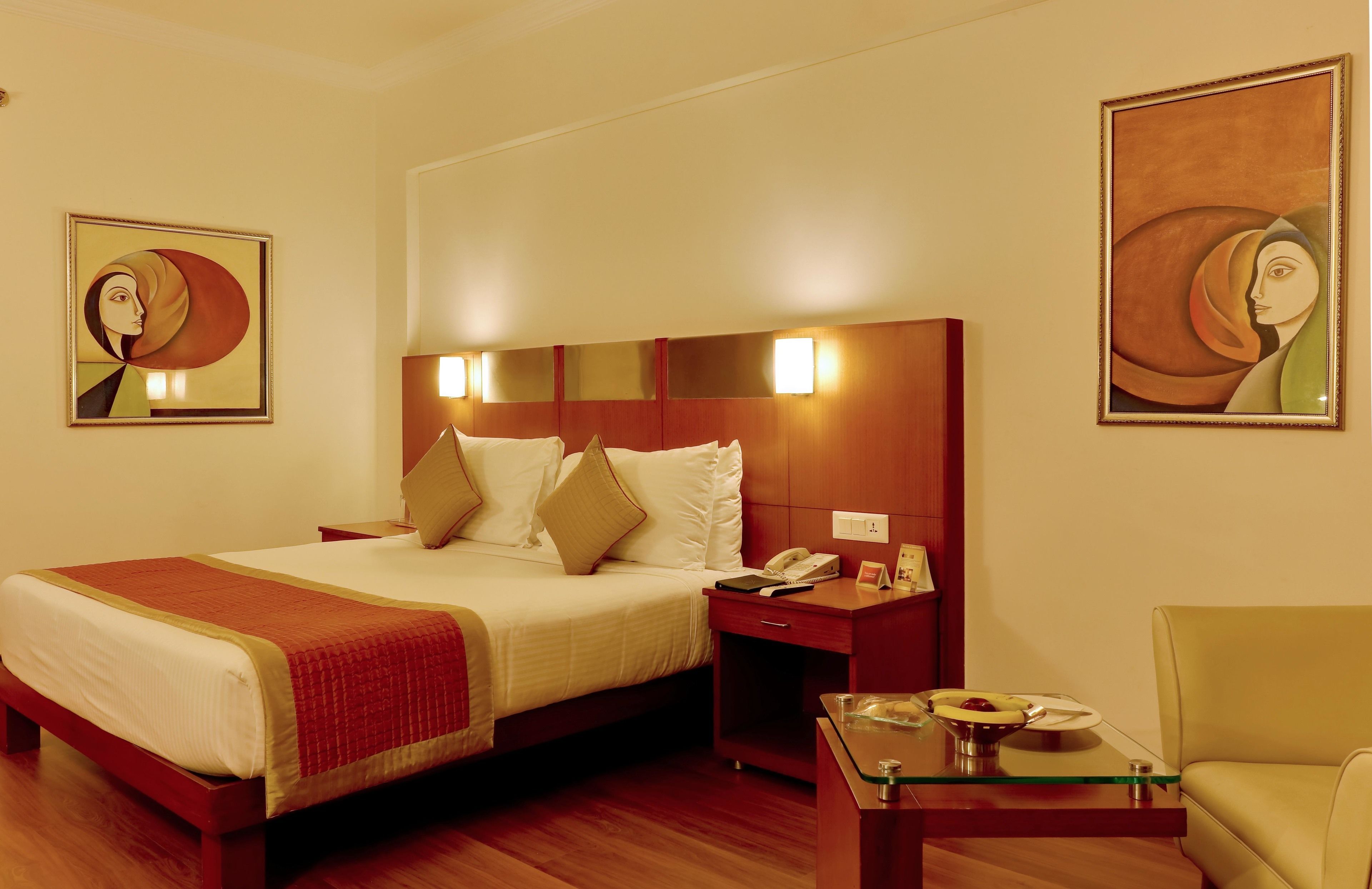 Habitación de hotel con una cama grande, mesitas de noche, una mesa de centro de vidrio y dos cuadros en las paredes.