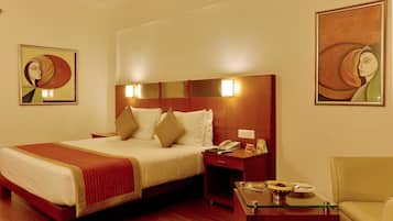 A hotel room with a large bed, bedside tables, a glass coffee table, and two paintings on the walls.