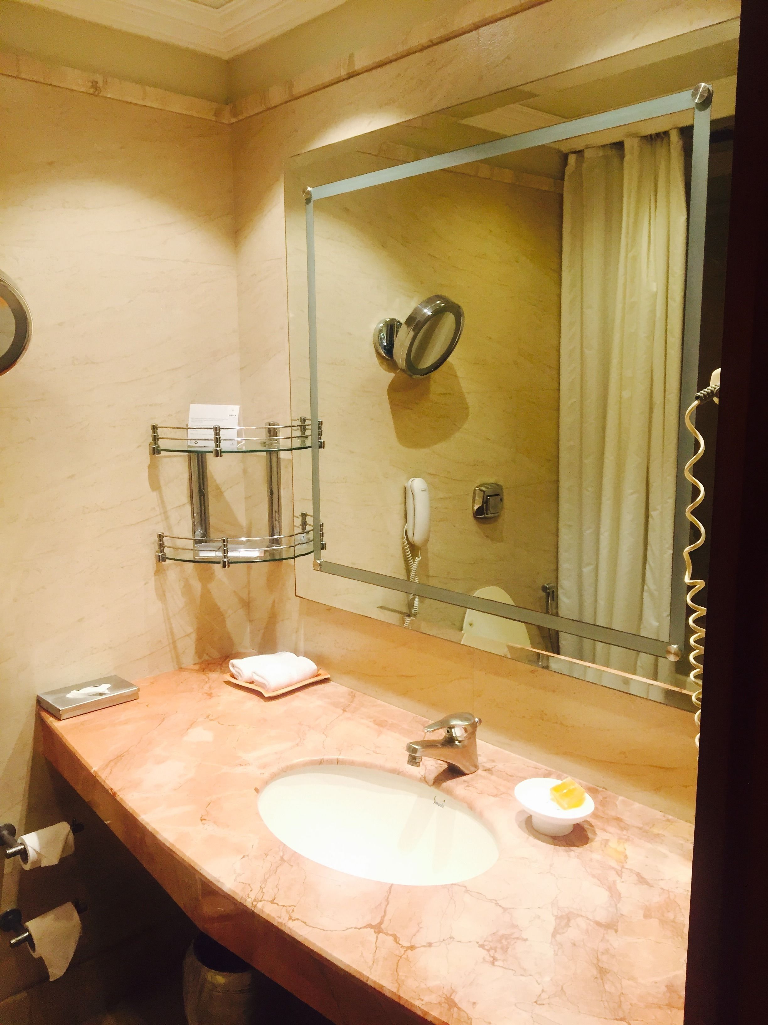 A bathroom with a marble sink, a mirror, a glass soap dish, a towel, and a toilet paper holder.