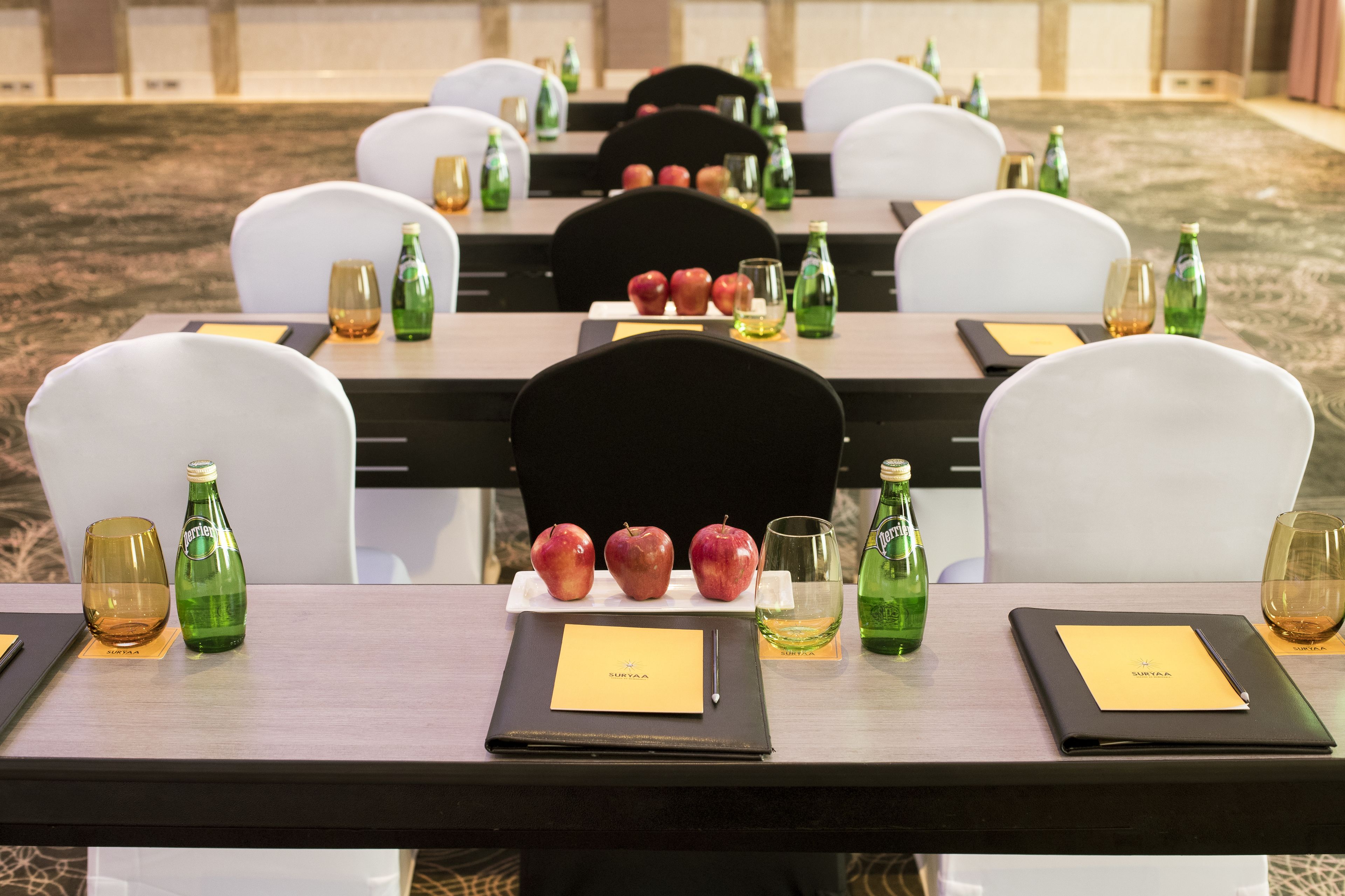 A dining table set with chairs, a bottle of water, a bottle of wine, a glass, and a plate with apples.