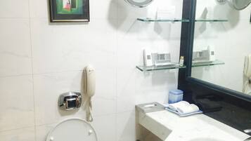 A bathroom with a toilet, a sink, a mirror, a framed painting, and a trash can.