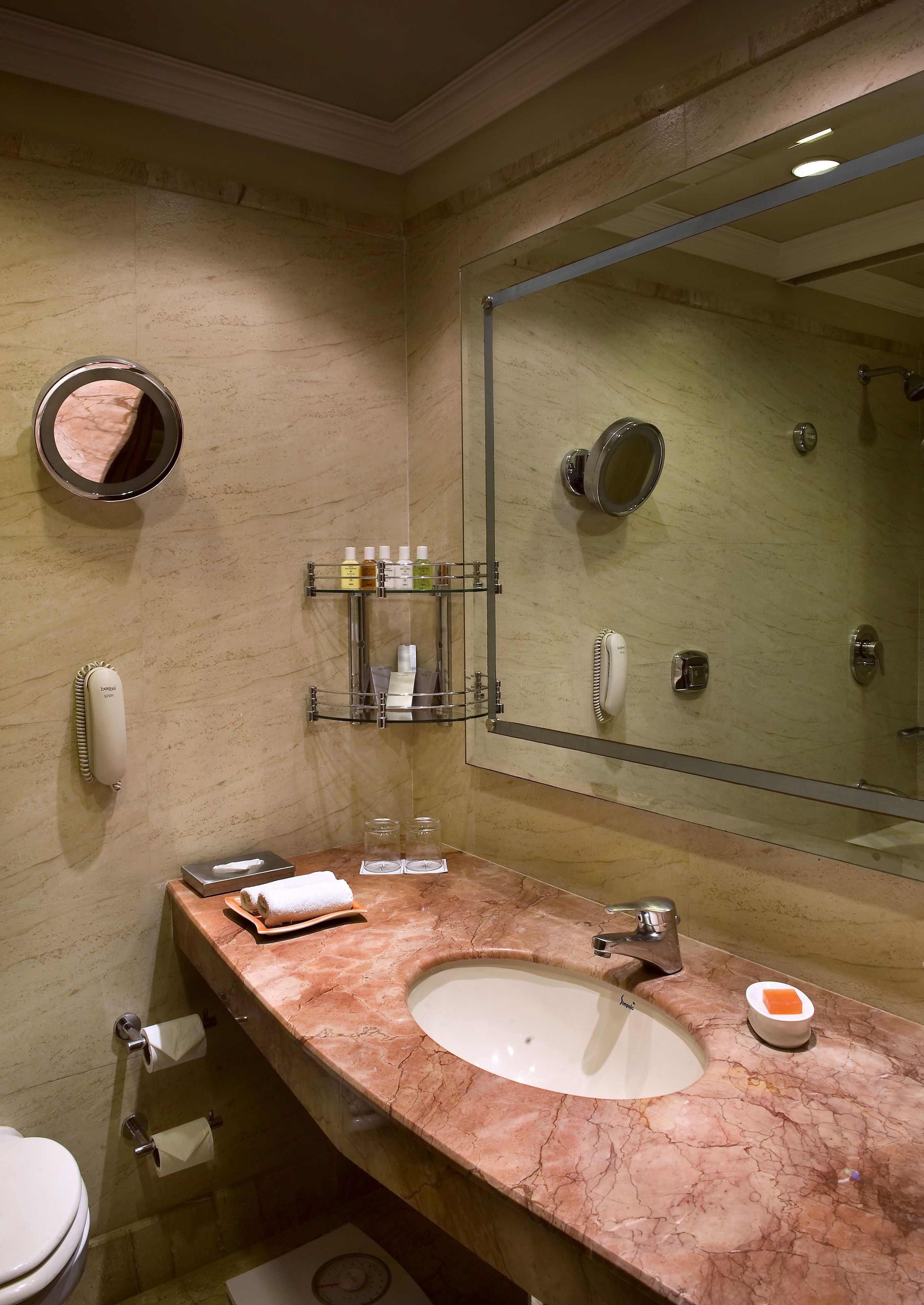 Un baño con lavamanos de mármol, un espejo grande, un perchero y un estante con artículos de aseo.
