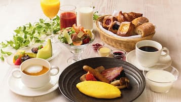 A breakfast setting with various food items, drinks, and a basket of pastries.