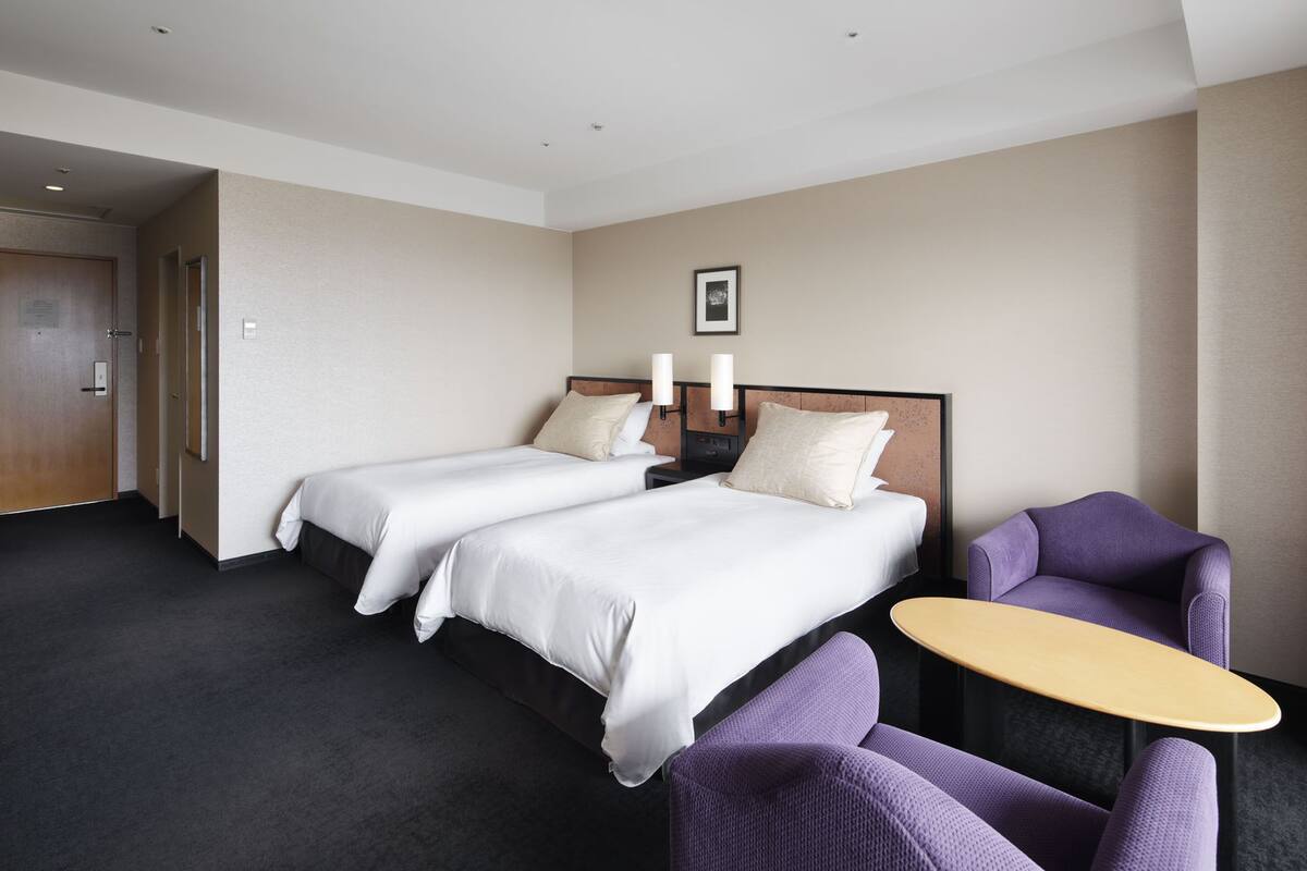Una habitación de hotel con dos camas, una mesita pequeña y sillas moradas.