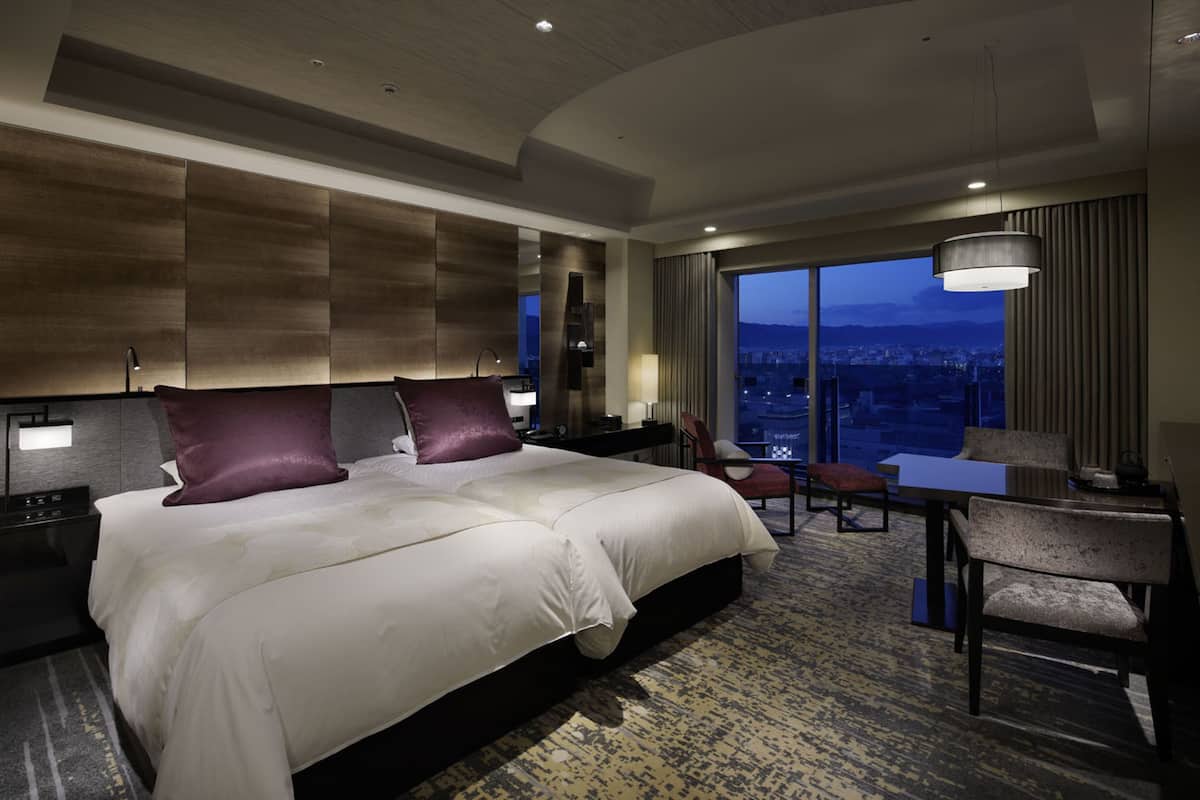 Una habitación de hotel moderna con una cama grande, un escritorio y vistas a la ciudad al anochecer.